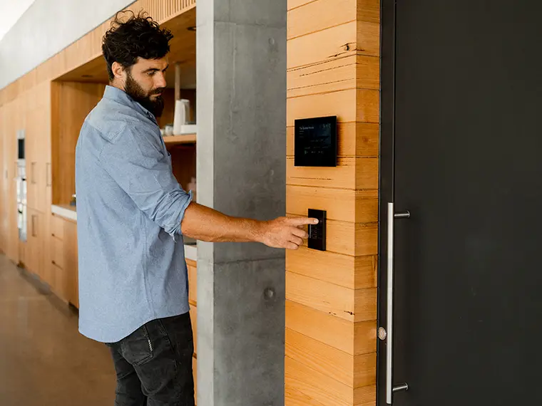 Person using a wall-mounted C-Bus panel on a wooden wall near a door.