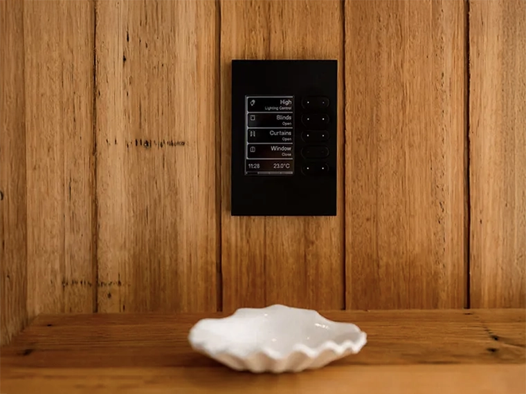 Smart home control panel on a wooden wall above a small white dish.