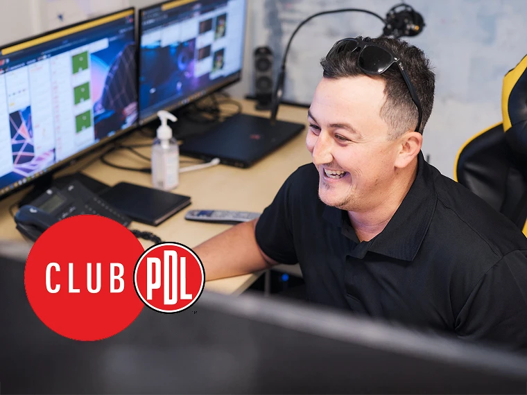 Person at a desk using multiple monitors in an office with visible Club PDL branding.