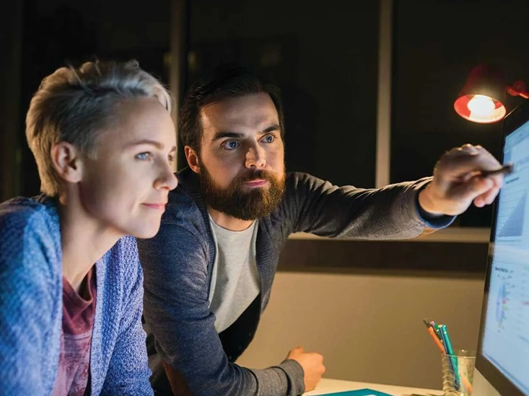 Two people reviewing data on a computer screen in an office.