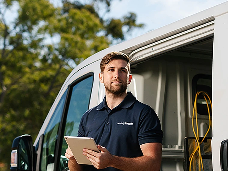 An electrician with a Schneider Electric branded work shirt leaning on a work van.