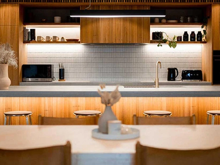 A warm, modern kitchen with wooden cabinetry, open shelving, and soft under‑cupboard lighting.
