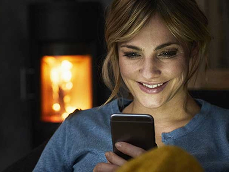A woman smiles at her smartphone while sitting in a living room.