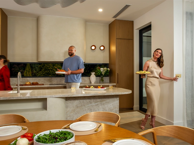People preparing and serving food in a modern kitchen with a large island and wooden cabinetry.