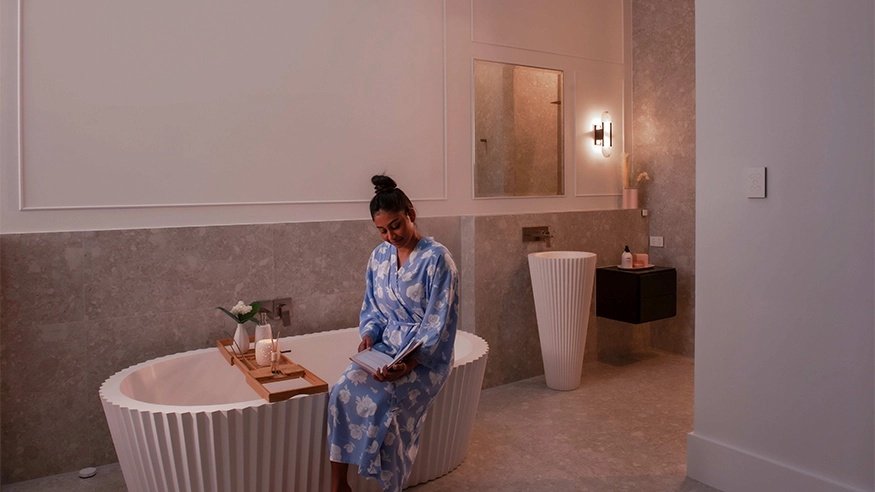 A woman sits in a bathtub surrounded by calming decor and soft lighting.