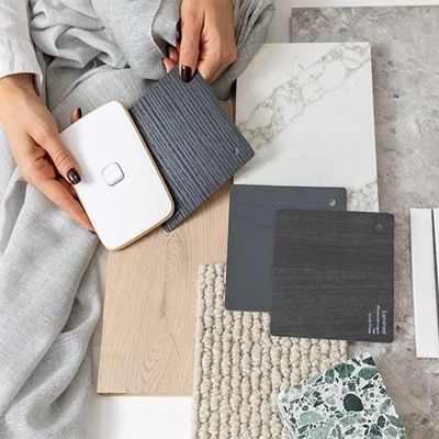 Hands holding colour and material samples, including a Iconic switch, fabric swatches, and stone tiles.