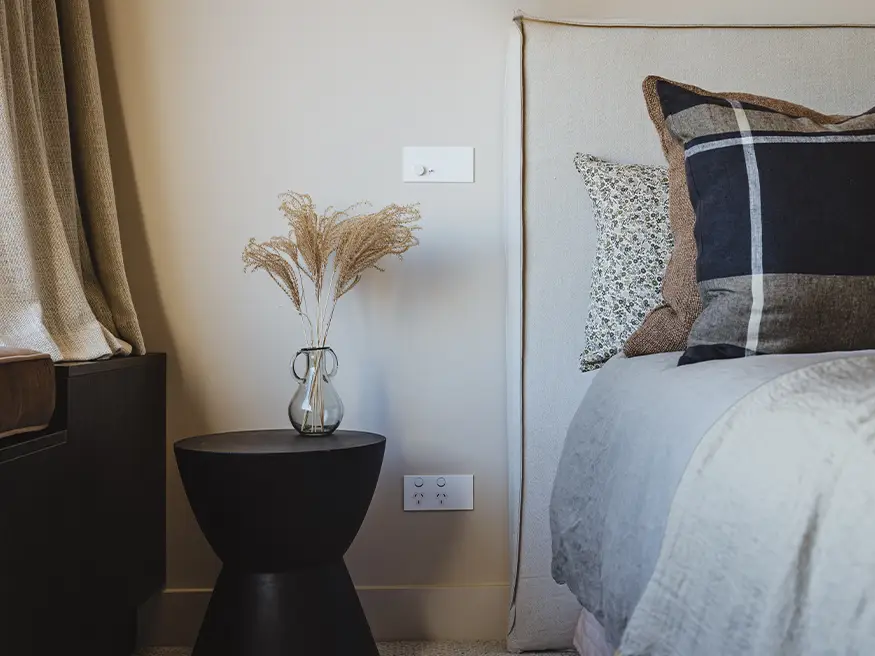 A white Solis switch and power outlet installed next to a bed.