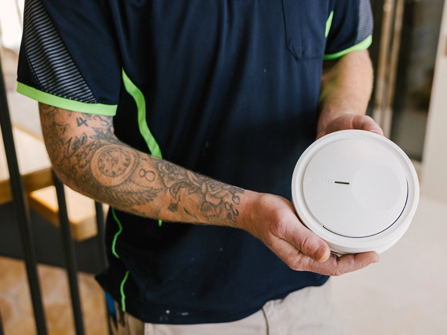 An electrician holding a PDL Fire Tek Smoke Alarm.