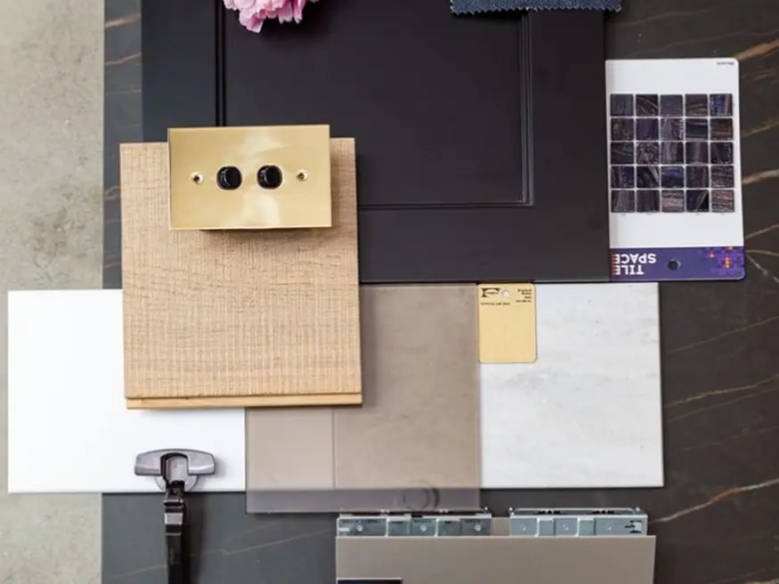 Metal switch plate with two black knobs among assorted interior design samples and tile swatches.