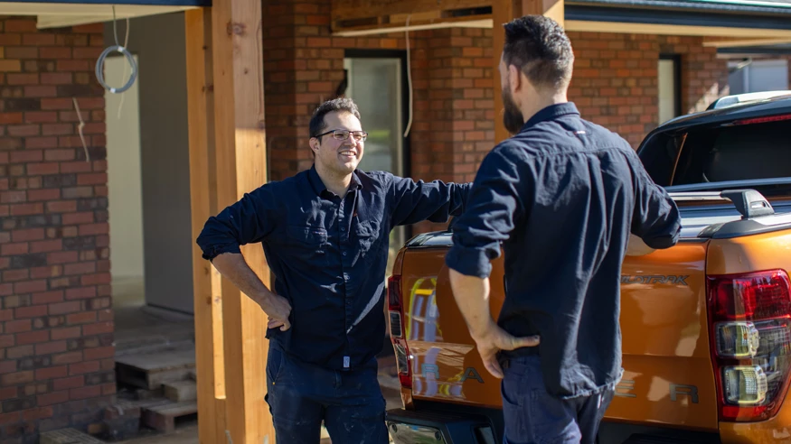 Two electricians having a conversation next to an orange work truck.