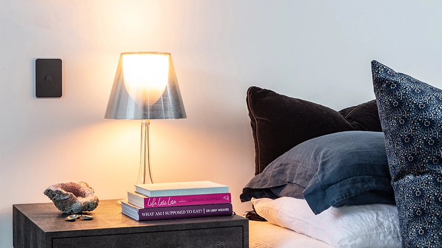 Cozy bedroom setup with a bedside table, lamp, books, and a wall-mounted PDL Iconic power point.