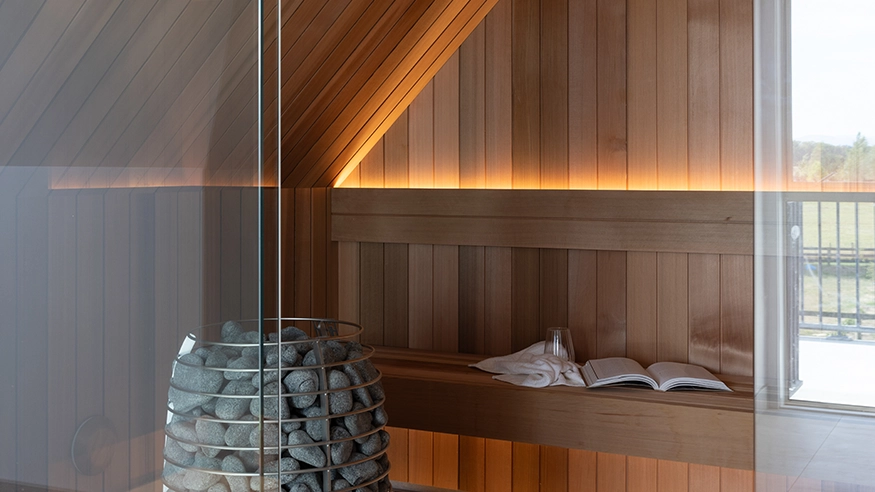 Modern sauna room with warm wooden panelling and a stone-filled heater.