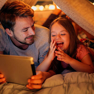 Father and daughter on ipad in a blanket fort.