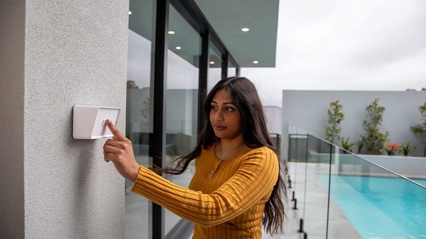 A woman controlling outdoor fans and garden lighting using a wall-mounted Iconic Outdoor switch.