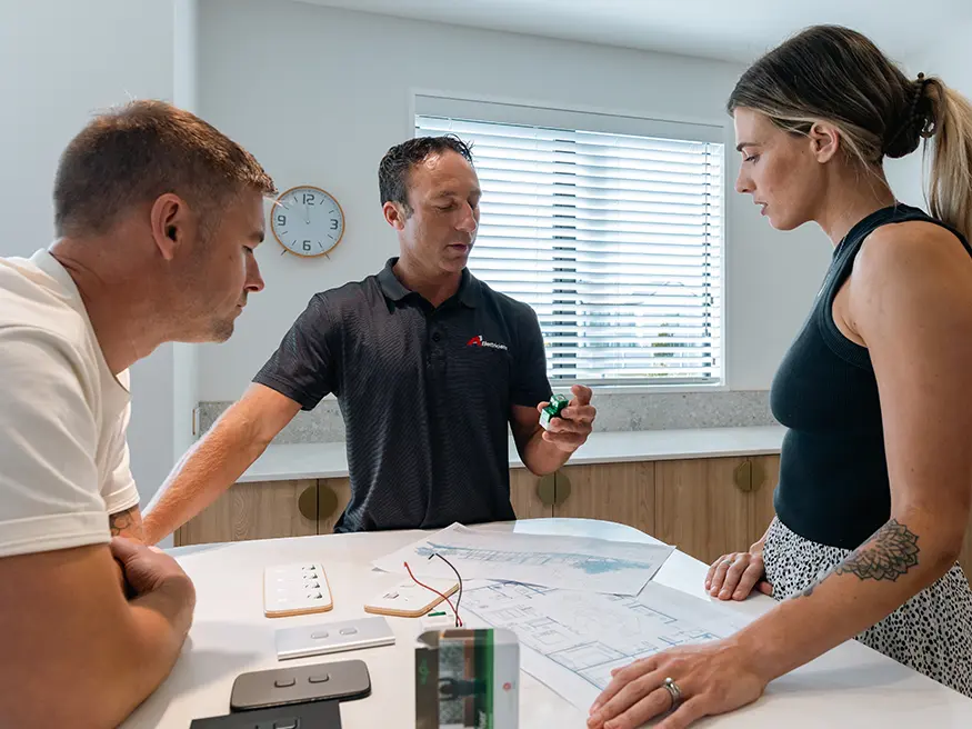 Three people discuss blueprints on a kitchen counter.