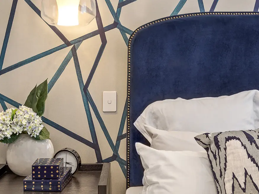 Iconic vivid white switch on a blue geometric wall above a bedroom nightstand.