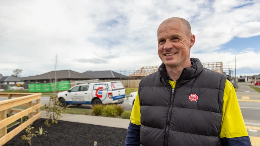 An electrician from Christchurch Electrical wearing a PDL branded vest smiles at the camera.