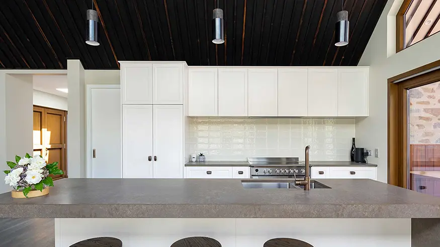 Modern kitchen with white cabinets, dark wood ceiling, and gray island countertop with sink.