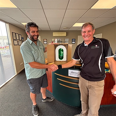 An electrician in a PDL shirt and a Club PDL staff member shaking hands and inspecting a PDL EV Charger from a member-only giveaway.