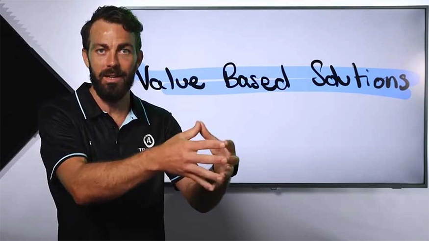 Presenter gesturing next to a screen showing “Value Based Solutions.”