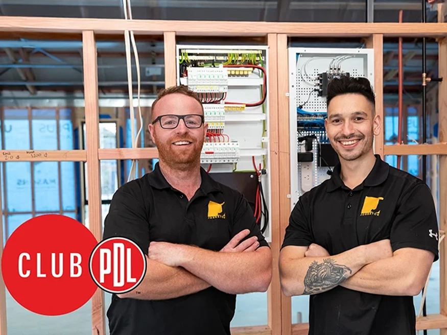 Two smiling electricians standing in front of a PDL Resi9 switchboard at aproject installation site.