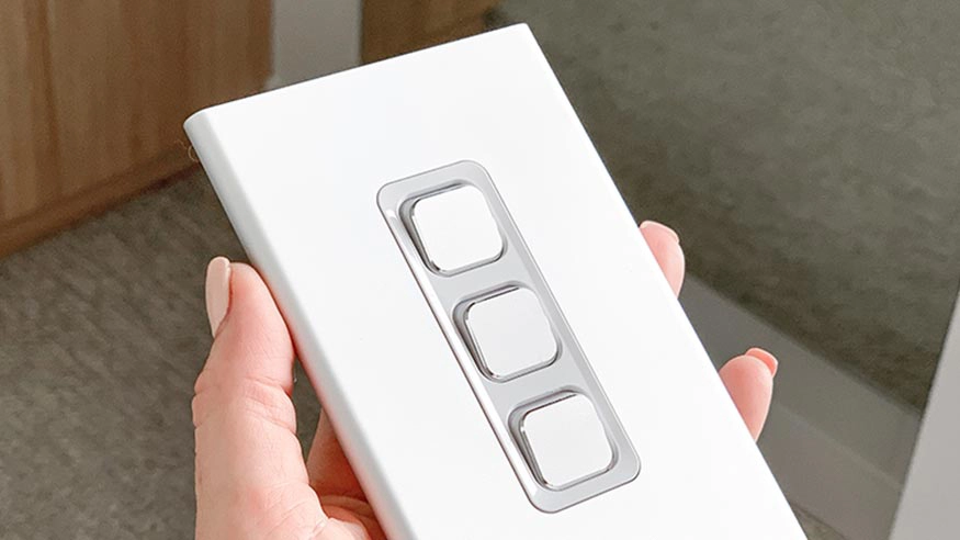 A hand holding a PDL Iconic styl vertical/horizontal switch with 3 gangs, providing controls for lighting or other electrical devices