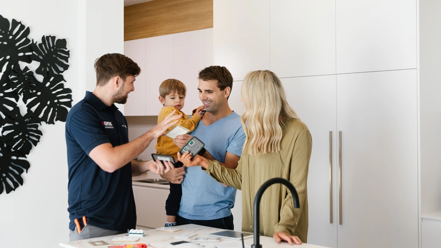 A family in conversation with a PDL electrician in their kitchen, with the father holding his son in his arms