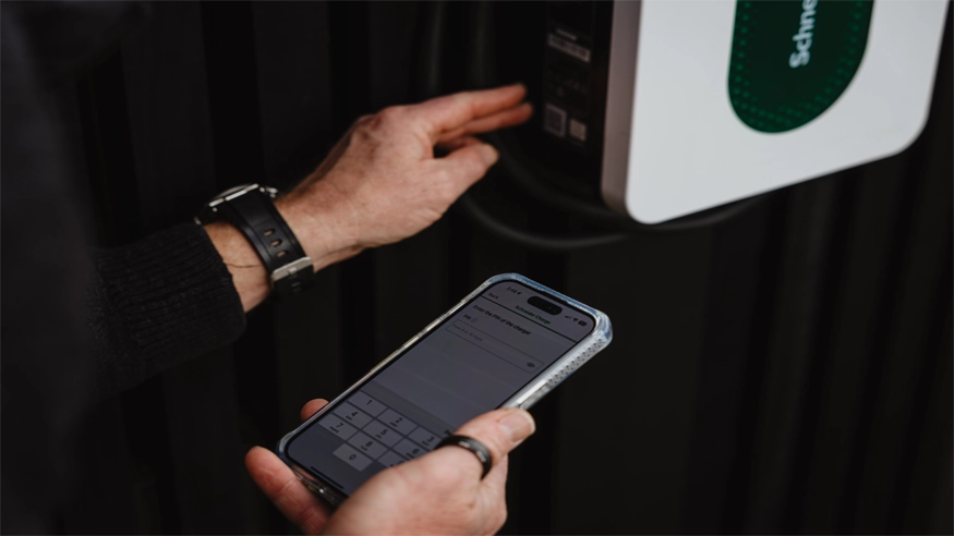 A user checks their Schneider Charge EV charger while viewing the Schneider Charge app on their smartphone.