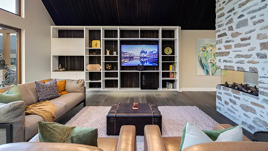Modern living room with sectional sofa, stone fireplace, and built-in shelves around a wall-mounted TV.