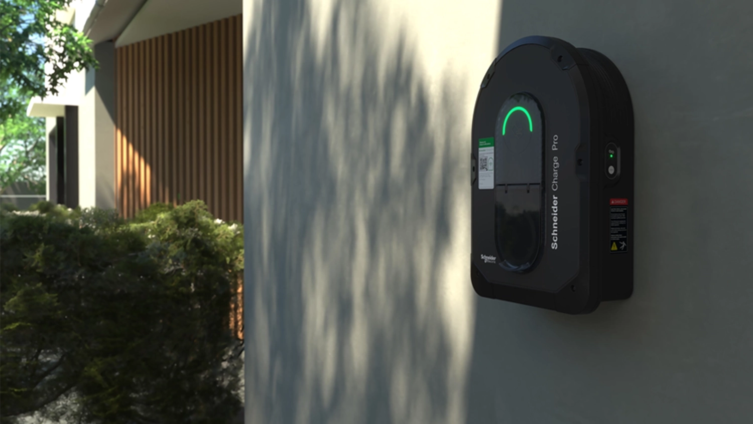 A Schneider Charge Pro EV charger wall-mounted on a white wall of a large modern house.
