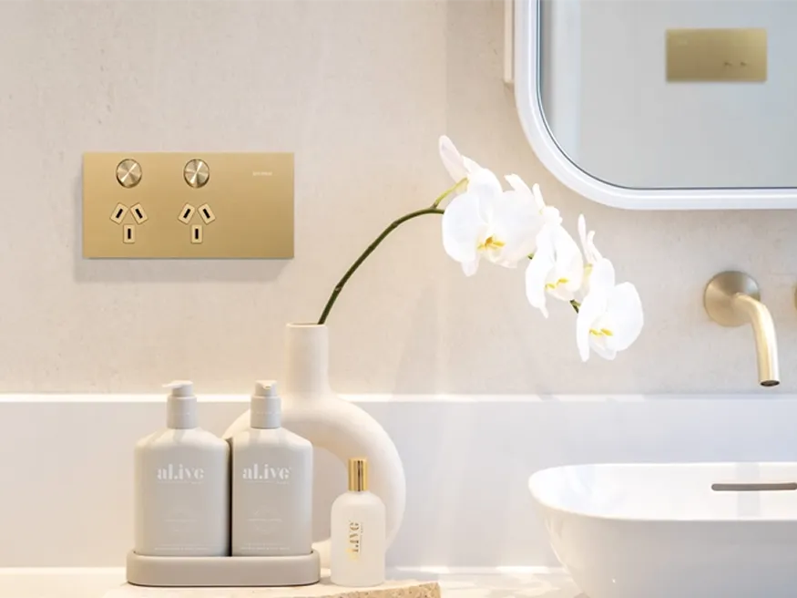 A Clipsal Solis T Series power outlet in brushed brass, installed in a bathroom.