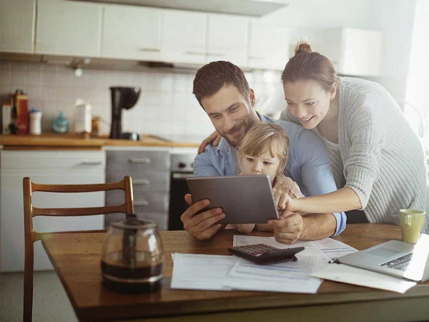 Adult and child viewing a tablet together at a kitchen table.