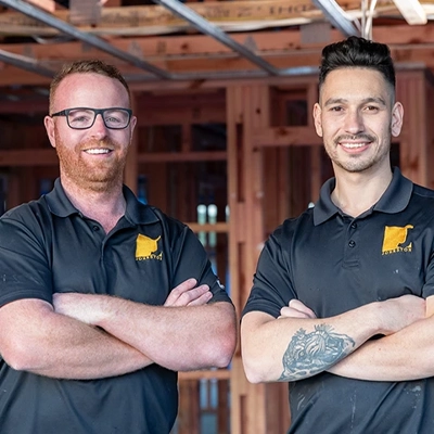 Two electricians standing inside a timber-framed construction site.
