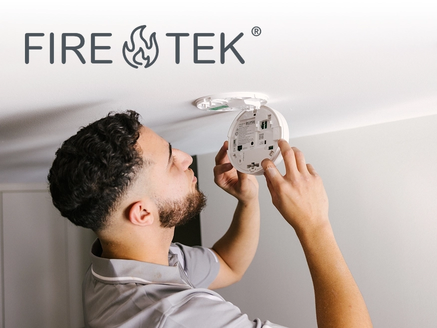 A photo of an electrician installing a Fire Tek Smoke Alarm branded with the Fire Tek logo.