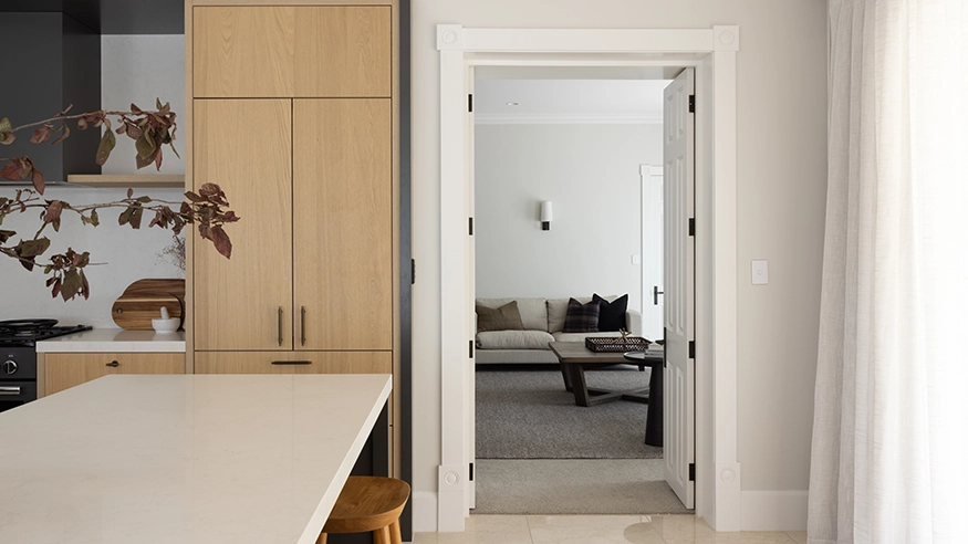 Modern Kitchen with light wood cabinetry and white countertops, leading to a cozy living room and features a Clipsal Iconic Switch on the wall.