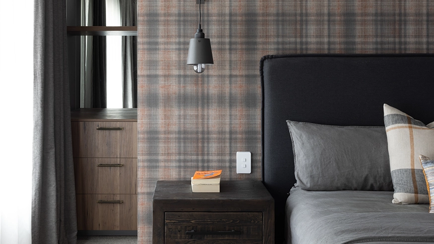 Modern bedroom with plaid wallpaper and grey bedding, showcasing a Clipsal Iconic Switch beside a nightstand.